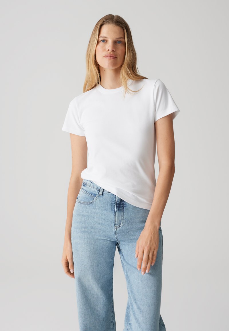 T-shirt bianco in cotone con maniche corte, scollatura rotonda e vestibilità comoda, abbinato a jeans in denim azzurro chiaro a vita alta.