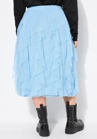 Gonna in tulle blu chiaro a strati con bordi arricciati, dotata di una vita elasticizzata. Indossata con stivali alla caviglia neri con borchie.