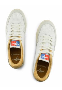 Sneakers bianchi con tomaia perforata, dettagli in pelle marrone chiaro e lacci piatti. Presentano il logo sulla lingua e un interno imbottito.
