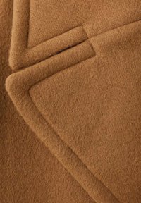 Tejido de lana marrón con una superficie suave y texturizada. Presenta esquinas dobladas y una apariencia uniforme, destacando su calidez y grosor.