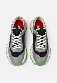Schwarze und graue Textil- und Gummisneaker mit grünen Sohlen, weißen Schnürsenkeln und roten Innensohlen, die eine abgerundete Zehenpartie und ein robustes Design aufweisen.