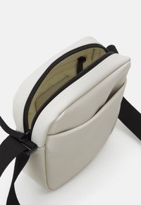 Torebka crossbody w miękkim, jasnoszarym materiale o gładkim wykończeniu. Posiada zamek błyskawiczny na górze, wewnętrzną kieszeń oraz czarny, regulowany pasek.