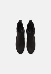 Bottines noires en daim lisse avec un design minimaliste, dotées d'une languette à l'arrière et sans éléments métalliques apparents ni ornements.
