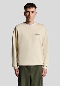 Felpa di colore crema chiaro con vestibilità rilassata, polsini a coste e scollatura a girocollo. Presenta il logo nero "LYLE & SCOTT" sul petto.