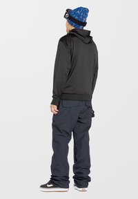 Sudadera negra de tejido suave, combinada con pantalones anchos azul oscuro y zapatillas negras. El gorro azul presenta un patrón en contraste.