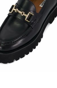 Zwarte leren instapper met een stevige rubberen zool. Kenmerkt zich door een goudkleurige gesp als accent en zijnaaddetails. Glad textuur overal.