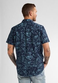 Camicia a maniche corte con sfondo blu navy e stampa botanica in tonalità teal. Realizzata in tessuto leggero con una vestibilità casual e orlo curvo.