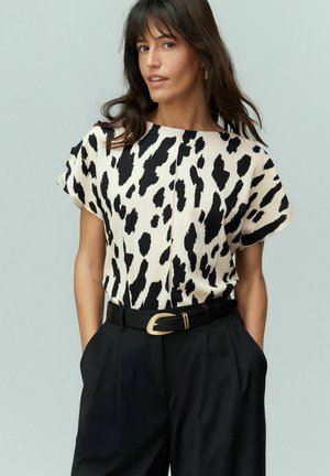 Top a maniche corte color crema con motivo animalier nero; tessuto testurizzato; abbinato a pantaloni neri a vita alta e a una cintura nera.