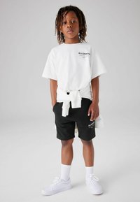 Vit t-shirt med kort ärm och logotyp, svarta shorts med logotyp, vita sneakers och vita knästrumpor. En enkel, avslappnad outfit.