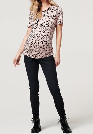 Top de maternidad en suave tela rosa, con estampado de leopardo negro y escote negro en contraste. Combinado con jeans negros ajustados y botas negras.
