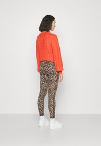 Pletena narančasta džemper s teksturiranim uzorkom, uparen s smešastim tajicama s leopard uzorkom i bijelim platformskim tenisicama.