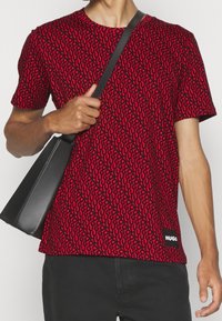 Camiseta roja de manga corta con un patrón abstracto negro, escote redondo y una etiqueta negra en el lado izquierdo. Textura de tela suave.