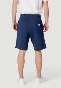 Pantalones cortos azul marino con un corte relajado, cinturilla elástica y un bolsillo trasero que presenta una pequeña etiqueta con el logo. Tela de algodón suave, de longitud por encima de la rodilla.