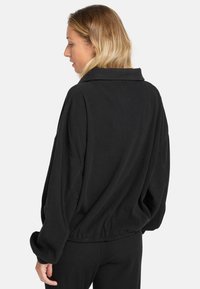 Zwarte geribbelde oversized jas met een brede kraag, verlaagde schouders en elastische zoom, ontworpen voor een relaxte pasvorm en comfort.