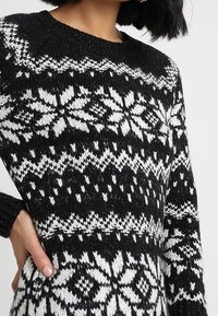 Maglione a righe in bianco e nero con collo a giro, maniche lunghe e intricati disegni a fiocchi di neve in morbido materiale a maglia testurizzata.