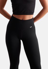 Black ribbed leggings with a high waistband, featuring a smooth texture and a small brand tag on the side.