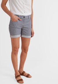 Shorts de mezclilla a rayas en azul marino y blanco, con un dobladillo vuelto, bolsillos frontales y cierre de botón. Combinados con sandalias marrones.