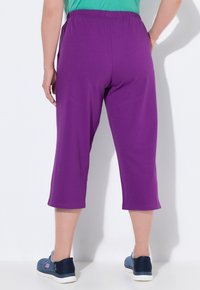 Paarse capri-pantalons met een elastische tailleband, gemaakt van zachte stof. G gedragen met blauwe sneakers, die een gladde textuur en rechte snit tonen.