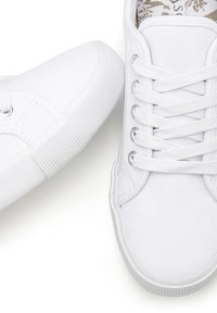 White canvas sneakers featuring a rounded toe, textured rubber sole, and flat laces with metal eyelets. Interior has a floral pattern.