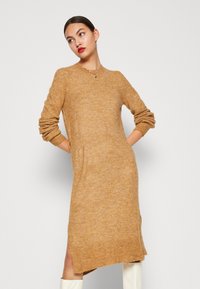 Rochie tricotată de culoare muștar, cu mâneci lungi, decolteu rotund, slituri laterale și o croială lejeră, realizată dintr-un material cu fir texturat.