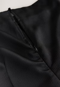 Close-up of a black textured fabric with a partially closed black zipper in the center on a light background.