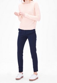 Maglione a maglia testurizzato rosa chiaro, pantaloni navy su misura con risvolti e sneaker bianche con suola chiara. Design minimalista, stile casual.