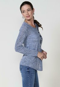 Hosszú ujjú kék melírozott felső fekete virágmintával, kerek nyakkivágással és laza szabással, kék farmerral párosítva. Sima textúra.