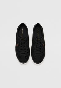 Paire de baskets noires Tommy Hilfiger avec dessus en mesh, lacets noirs et semelles blanches sur fond blanc.