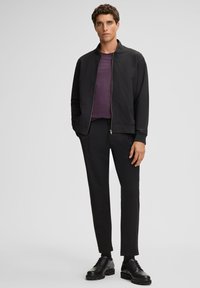 Zwarte zip-up jas, paarse shirt, zwarte slim-fit broek. Glad stof, minimalistisch design, subtiele textuur, afgewerkt met zwarte schoenen.