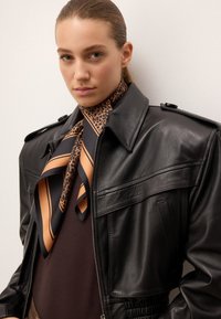 Svart läderjacka med knäppbar krage, sidofickor och texturerad finish. I kombination med en mönstrad orange och svart silkesjaal.