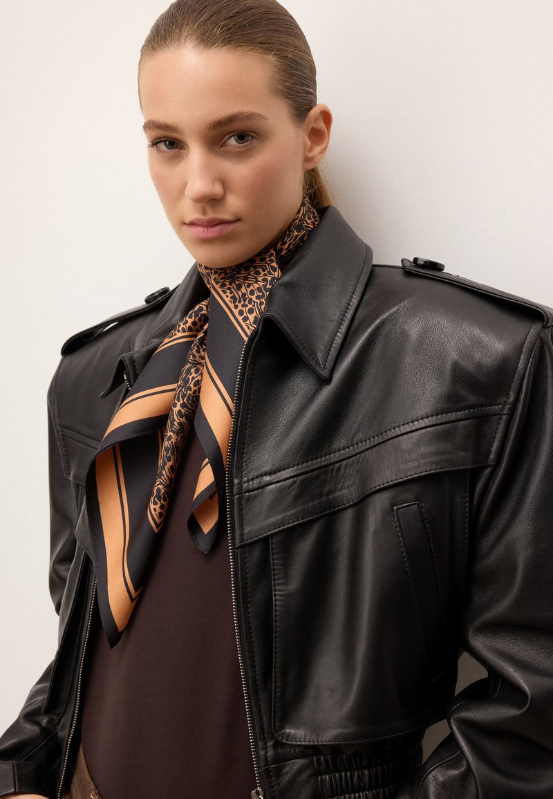 Svart läderjacka med knäppbar krage, sidofickor och texturerad finish. I kombination med en mönstrad orange och svart silkesjaal.