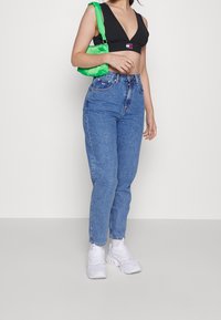 Hög midja blå denim jeans, avslappnad passform, lätt tapered ben. Bärs med en svart kort ovan del och en ljusgrön väska, tillsammans med vita sneakers.