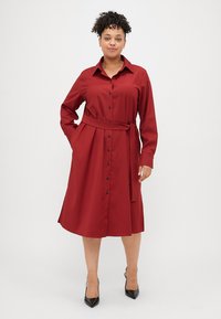 Vestido camisa vermelho de mangas longas, feito de um tecido suave, apresentando uma frente com botões, cinto na cintura e um corte descontraído em forma de A.