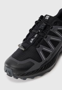 Black and gray trail running shoe with textured toe, quick-lace system, and "SALOMON" branding on tongue and lace lock.