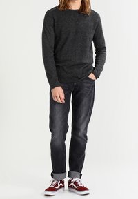 Dunkelgrauer Langarmpullover, kombiniert mit leicht hochgerollten dunklen Jeans und bordeauxfarbenen Sneakers mit weißen Akzenten. Einfaches, lässiges Design.