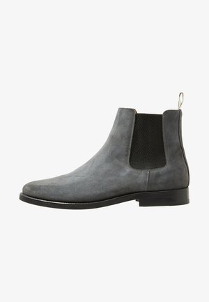 Bottine Chelsea en daim gris avec panneau latéral élastique noir et semelle noire, avec une languette à l’arrière.