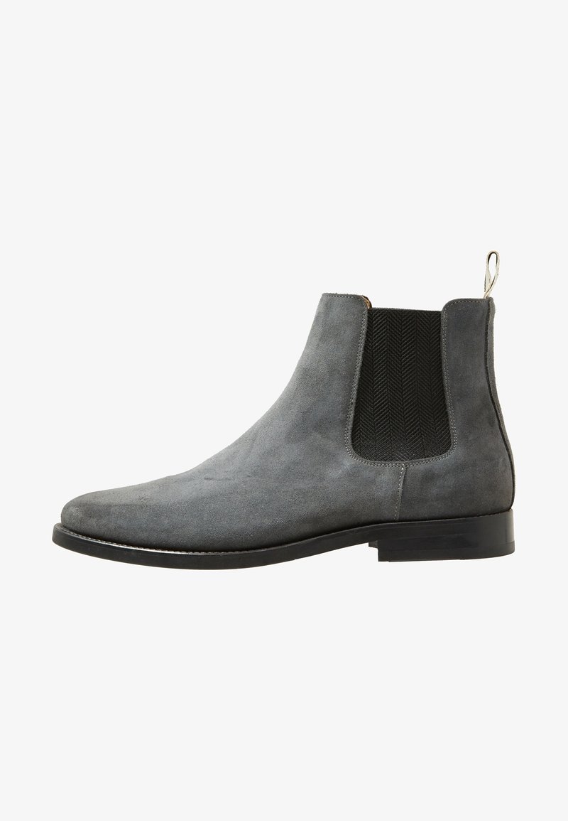 Bottine Chelsea en daim gris avec panneau latéral élastique noir et semelle noire, avec une languette à l’arrière.