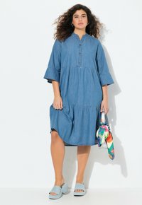 Denim-mekko, jossa on napitettava etumus, kolmanneksen mittaiset kellohelma hihat ja kerroksittain laskostettu hame. Yhdistettynä sinisiin platform-sandaaleihin ja värikkääseen huiviin.