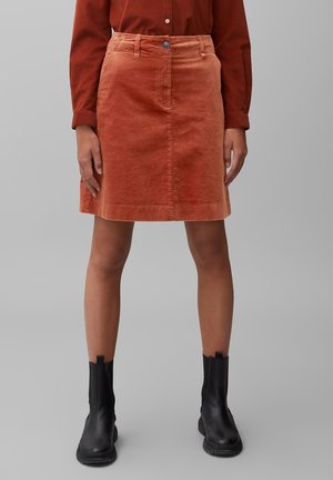 Jupe en velours côtelé orange brûlé, longueur genou avec poches avant, fermeture à boutons et design droit, associée à des bottines noires.