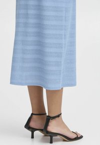 Rochie tricotată de culoare albastră deschisă cu dungi verticale; combinată cu sandale negre cu bretele, având un toc mic și curea la gleznă.