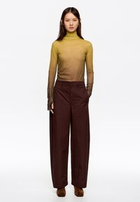 Poolik kollakas-roheline pikakätine kõrge kaelusega särk on kokku sobitatud kõrge vöökohtadega tumepunaste laiade pükste ja pruunide sametkõrgete saapadega.