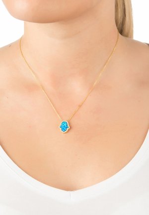 Collana d'oro con ciondolo a forma di mano blu, adornato con piccoli cristalli, che mostra un dettaglio intricato e una catena delicata.