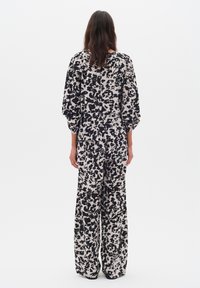 Salopetă cu mânecă lungă, având un model abstract în nuanțe de negru și crem, pantaloni largi și o croială lejeră, realizată dintr-un material moale și texturat.