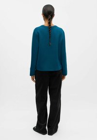 Tealfärgad sweatshirt med långa ärmar, rund halsringning och en avslappnad passform. Kombinerad med svarta kordbyxor. Minimalistisk design utan synliga mönster.