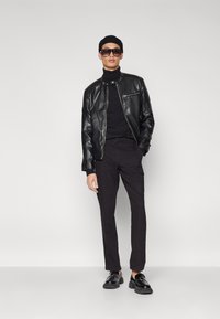 Chaqueta bomber de cuero negra sobre un cuello de tortuga negro, combinada con pantalones cargo negros y mocasines negros, complementada con gafas de sol negras de gran tamaño.