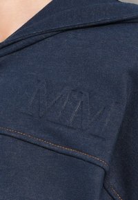 Felpa blu navy con un logo in rilievo distintivo e cuciture a contrasto, colletto rilassato e tessuto morbido e testurizzato.