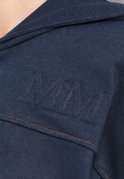 Sudadera azul marino con un distintivo logotipo en relieve y costuras en contraste, con un cuello relajado y una tela suave y texturizada.