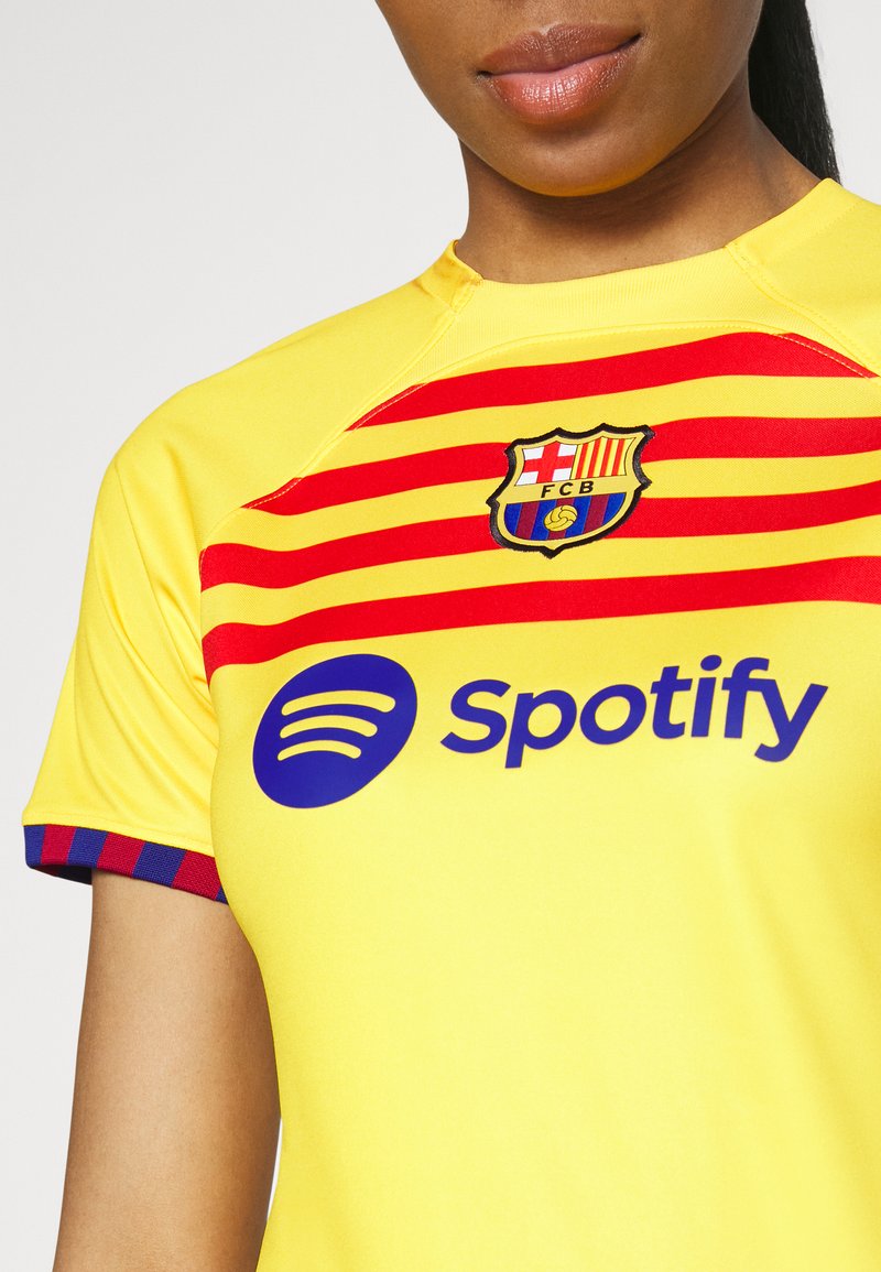 Camisa del FC Barcelona en amarillo, con rayas rojas y el escudo del club. Logo de "Spotify" en azul debajo. Mangas cortas con acentos a rayas.