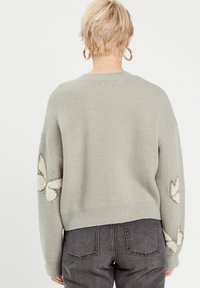 Sweater tricot gris avec des manches longues, un col rond et des motifs de papillons brodés sur les épaules. Texture douce et coupe décontractée.