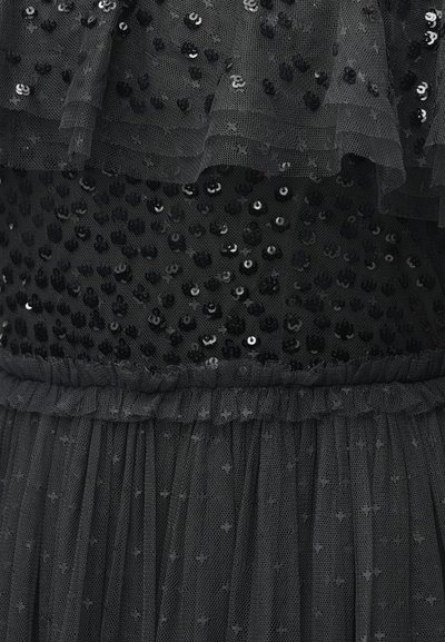 Robe en tulle noir avec volants superposés, ornée de paillettes noires. Présente une taille froncée et un tissu transparent texturé.